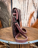   Side view of the Duskline Embossed Crossbody Purse displayed on a wooden table with wheat in the back ground, sitting in front of a wood back drop.