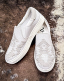 White slip-on sneakers with woven pattern on a textured brown and white surface