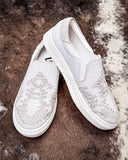 White slip-on sneakers with woven design on a textured brown and white surface