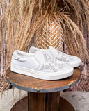 White slip-on sneakers with decorative elements on a wooden surface with a natural background