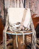 Beige handbag with fringe on a wooden stool against a rustic background