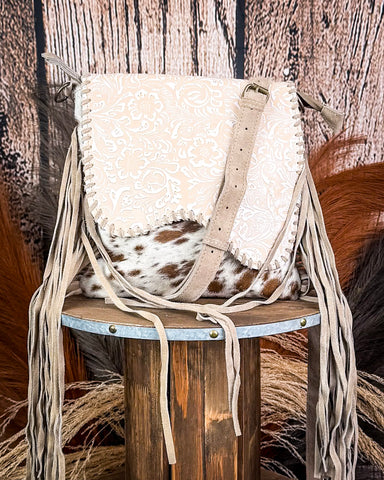Beige handbag with fringe on a wooden stool against a rustic background