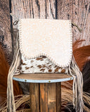 White embossed bag with fringe on a wooden stool against a rustic background