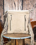 Beige leather bag with fringe on a wooden stool against a rustic background