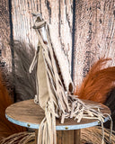 Beige leather bag with fringe on a wooden stand against a rustic background