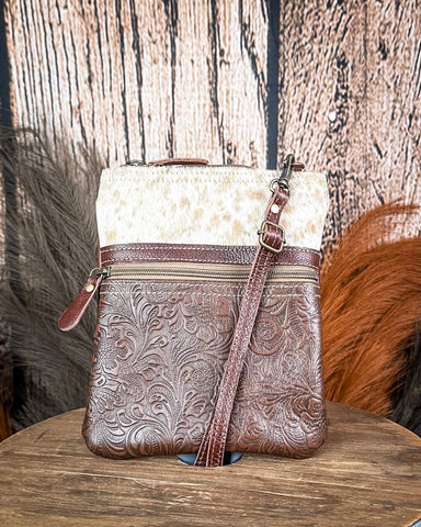 Brown leather handbag with floral patterns on a wooden surface