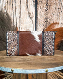 Brown leather clutch with floral tooling on a wooden surface