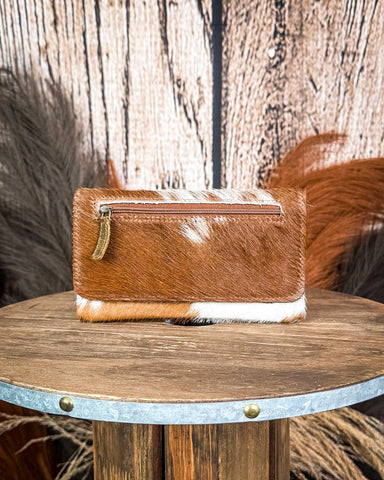 Brown and white cowhide wallet on a wooden surface with a rustic background