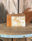 Brown and white cowhide wallet on a wooden surface with a rustic background