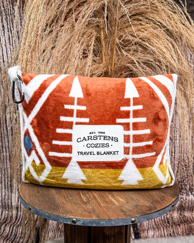 Travel blanket with southwestern pattern and Carstens Cozies branding on a wooden stool.