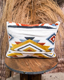 Travel blanket with geometric pattern on a wooden stool against a textured wall.