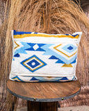 Travel blanket with blue and gold geometric pattern on a wooden stool against a rustic background
