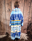 Person wearing a blue and white patterned hooded blanket against a wooden wall.