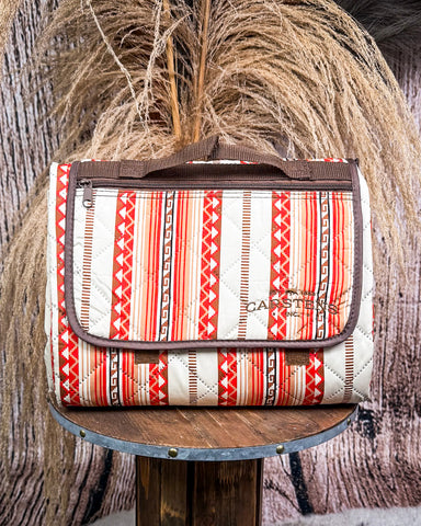 Picnic blanket with red and beige pattern on a wooden stand against a rustic background