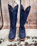 Pair of navy blue cowboy boots with brown soles on a textured surface.