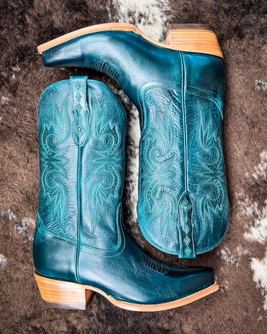 Pair of blue cowboy boots with intricate designs on a textured surface