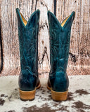 Pair of teal cowboy boots with brown soles on a wooden surface.