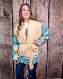 Woman wearing a patterned cardigan over a white shirt standing against a wooden background.