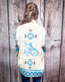 Person wearing a cream-colored cardigan with blue and brown patterns against a wooden background