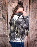 Person wearing a black and white fringed leather jacket against a wooden background