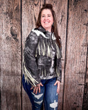 Woman wearing a fringed jacket and jeans standing against a wooden background
