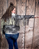 Person wearing a black fringe jacket against a wooden background