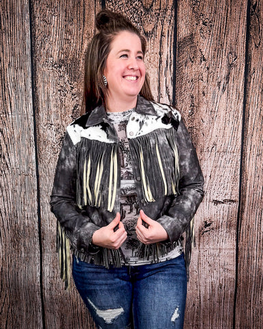 Person wearing a black and white patterned jacket with fringe against a wooden background