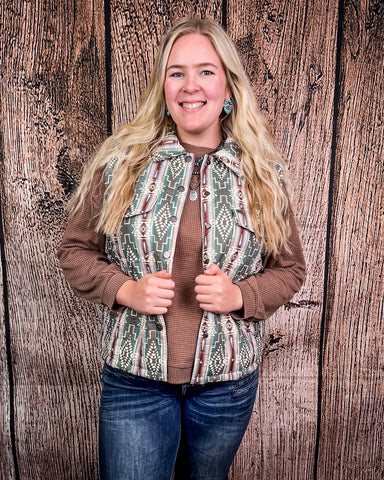Woman wearing a patterned vest over a brown sweater with a wooden background