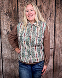 Person wearing a patterned vest over a long-sleeve shirt and jeans against a wooden background