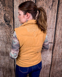 Woman wearing a beige puffer vest against a wooden background