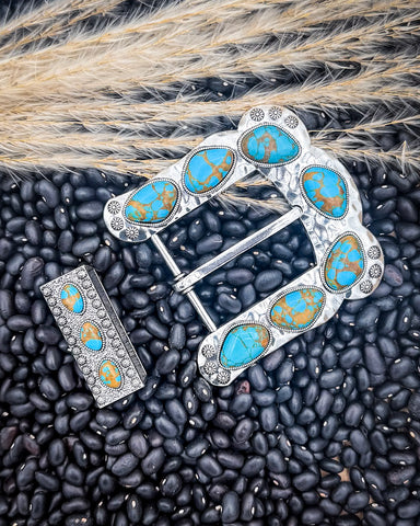 Silver and turquoise belt buckle displayed on black beans.