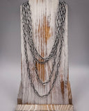 Stack of silver chain necklaces on a wooden block with a gray background