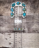 Silver and turquoise belt buckle on a ruler for size.