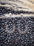 Pair of The Calico Drops earrings styled on black beans and wheat.