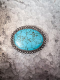Large oval turquoise Western belt buckle with floral silver border on tin background