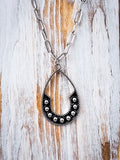 Close-up of silver teardrop horseshoe pendant on wood background – rustic Western jewelry