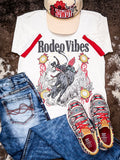 Flat lay Rodeo Vibes graphic tee with jeans, Howdy trucker hat, and Aztec sneakers