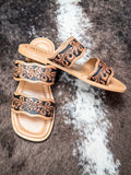 Tooled leather double-strap sandals with floral design on tan sole, displayed on faux cowhide rug.