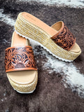 Pair of western-style sandals on faux fur surface, showing detailed floral tooling and jute sole.