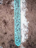 Close-up of floral embossed turquoise leather belt tip with intricate detailing.