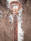 Tooled leather belt with floral design and engraved western buckle, laid on faux fur.