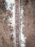 Close-up of brown tooled leather belt tip with floral western embossing on cowhide background.