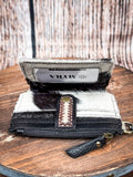 Cowhide wallet with clear ID slot and leather snap closure on rustic wood table.