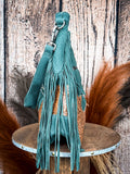 Side profile of green suede handbag with fringe tassels and engraved leather panel