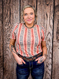 Smiling woman modeling peach and navy Aztec top with ruched shoulders and statement earrings.