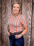 Woman in a short sleeve peach and navy western-style shirt with puff shoulders and dark denim.
