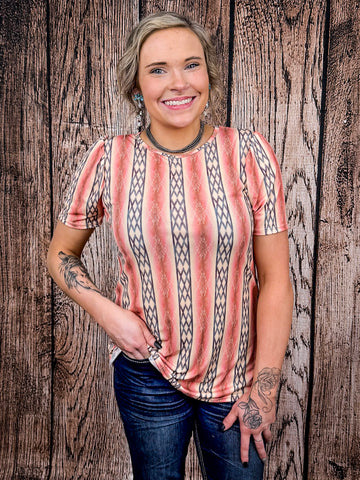 Front view of woman wearing peach and navy Aztec stripe puff sleeve top with dark wash denim jeans.