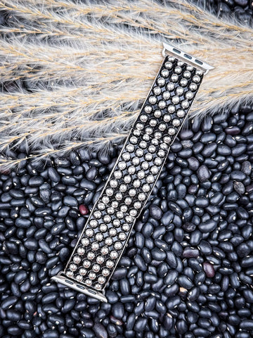 Angled silver Apple Watch band with multiple metal studs on organic black bean surface