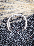 Curved silver Apple Watch band with raised dot detailing on rustic bean and grain background