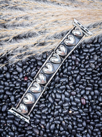 Angled view of heart-pattern silver Apple Watch band on textured bean and wheat surface